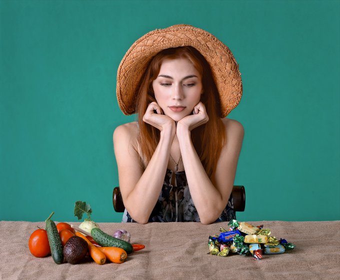 kobieta patrząca na warzywa i słodycze